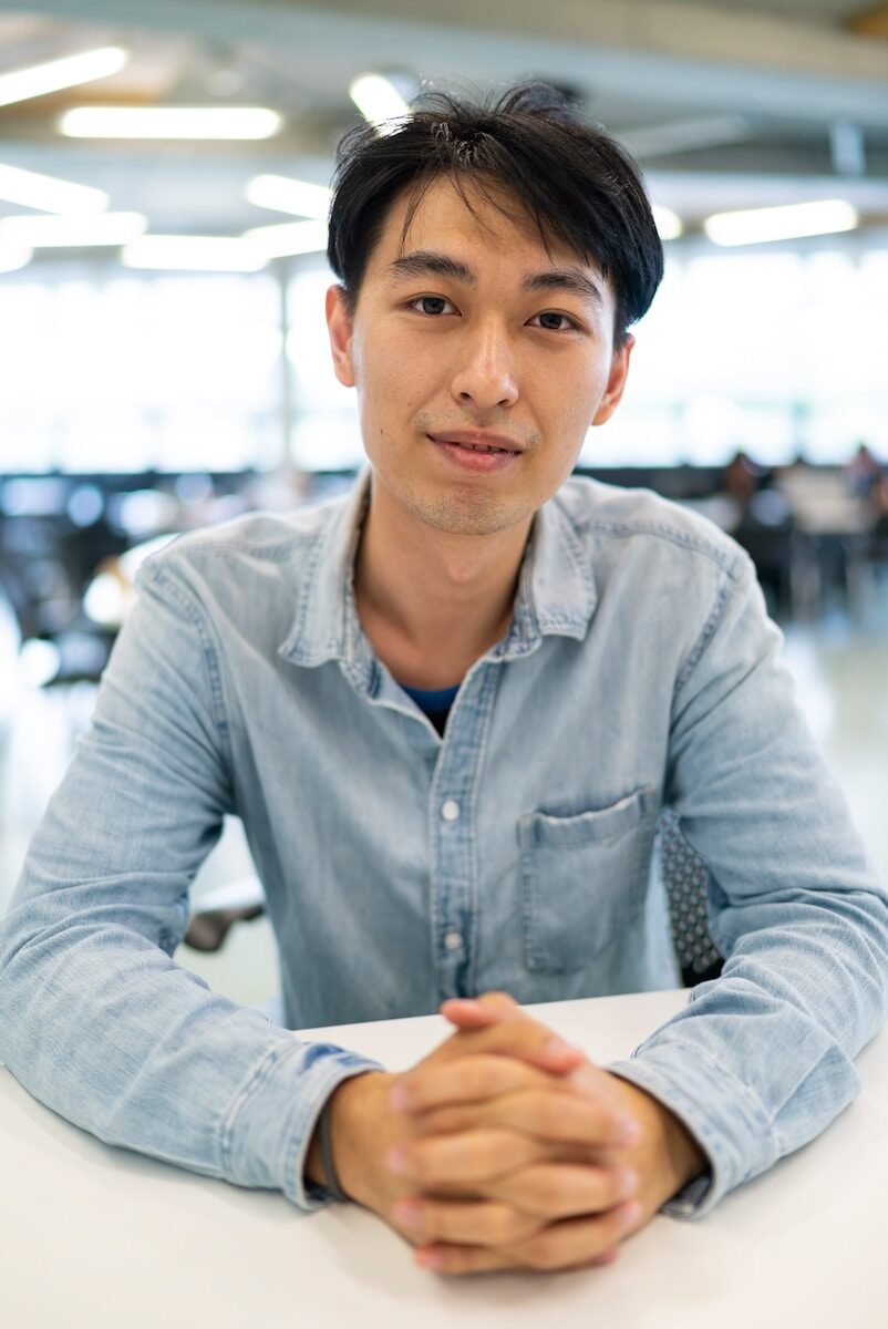 A man in a light blue denim shirt sitting at a white desk